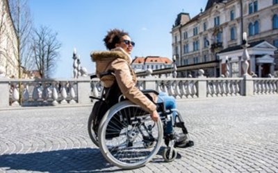 Junge Frau fährt mit Rollstuhl über eine Brücke